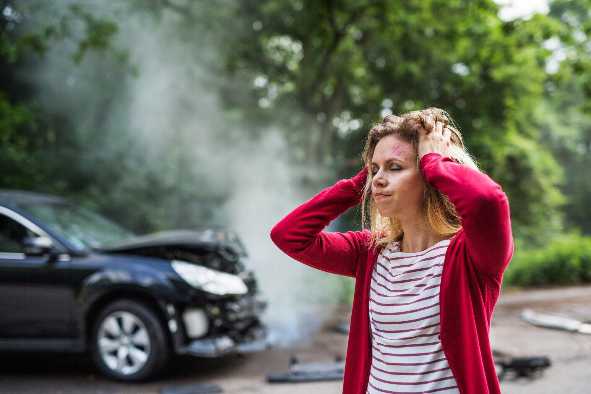 An injured young woman standing by a damaged car after a car accident. Used to illustrate the article - "How to Find a Reliable Body Shop Near You".