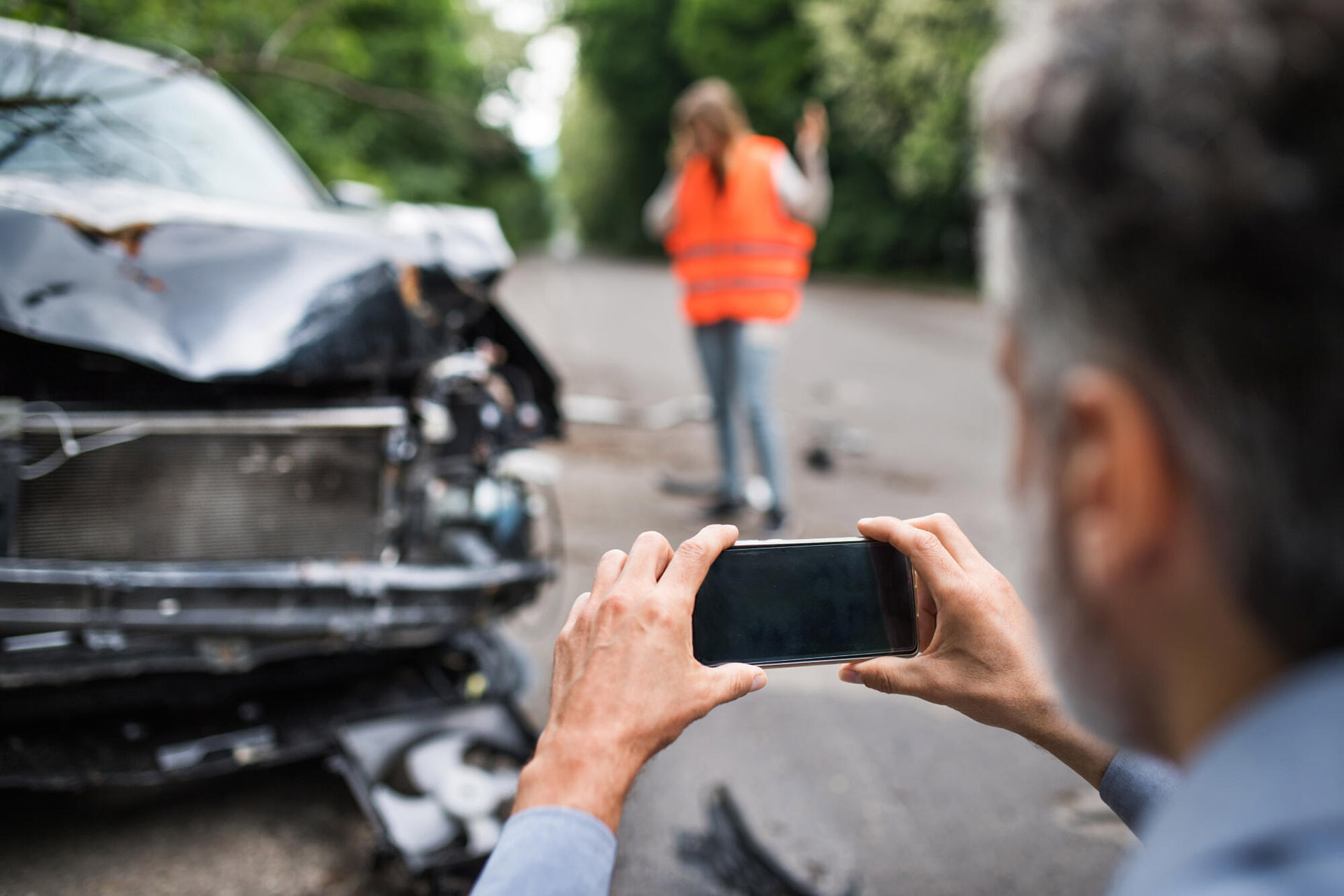 A man takes a photo of a car with structural damage following an accident.